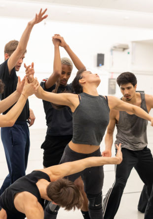 Un groupe de danseuses et danseurs en plein mouvement, portant des habits de répétitions.